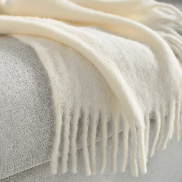 Fluffy, off-white throw blanket with fringes, draped softly, highlighting luxurious texture
