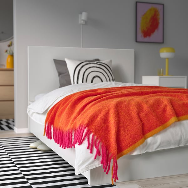 Bright pink & orange throw blanket, fluffy, recycled polyester, large, draped on white bed, larger than pillows.