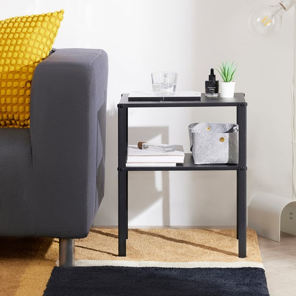 Black side table with glass, plant, books. Sleek metal design, modern decor.