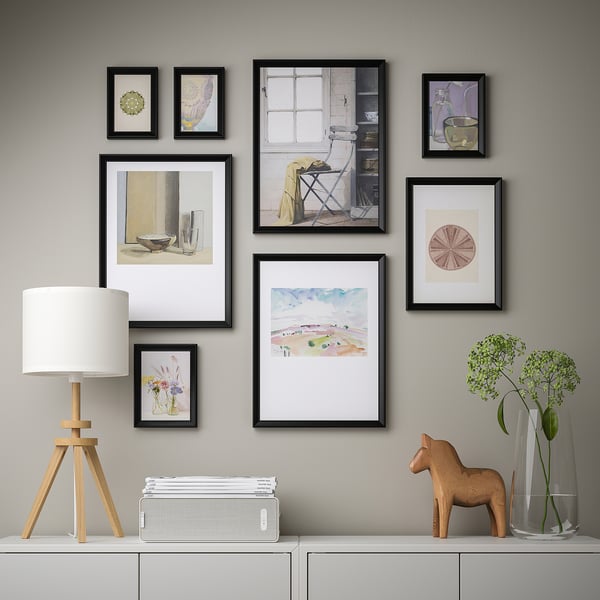 Gallery wall with various framed artworks, including a landscape painting, a lamp, a speaker, books, and decorative items, arranged neatly on a wall.