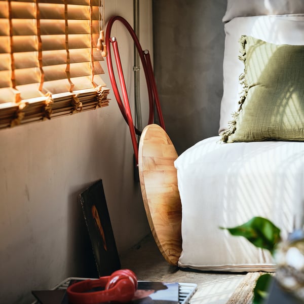 Foldable side table in red next to bed, easy to move. Wooden top, lean against wall or bed.