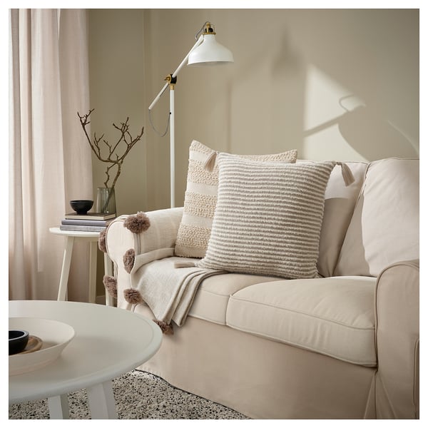 Calm living room with beige couch, beige cushions, white lamp, and side table.