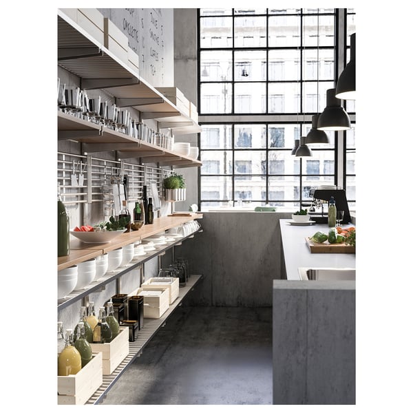 Modern industrial kitchen with stainless steel shelves, glassware, and hanging lamps overlooking cityscape windows.