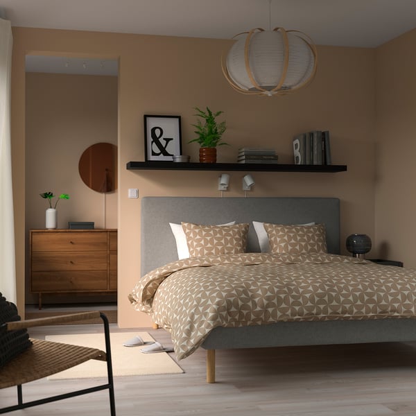 Bedroom with LACK shelf, plant, books, pendant light, wooden dresser, and unique bedding.
