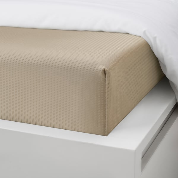 A fitted sheet with elastic edge on a white bed, showing its snug fit and smooth material.