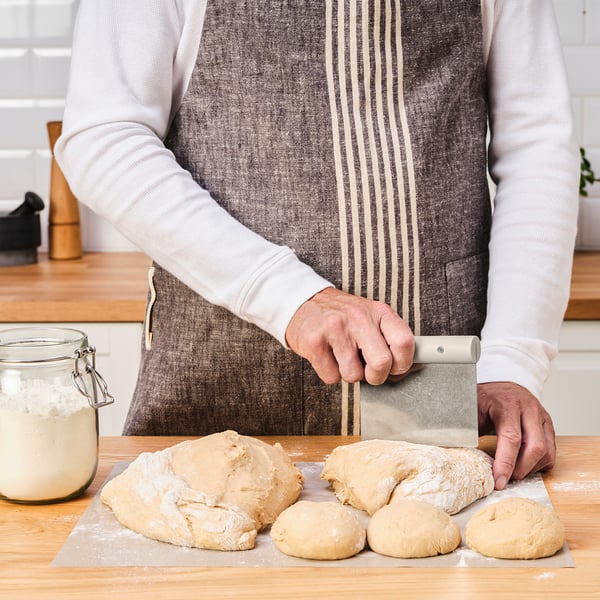 Person divides dough with a metal bench scraper on a floured wooden cutting board.