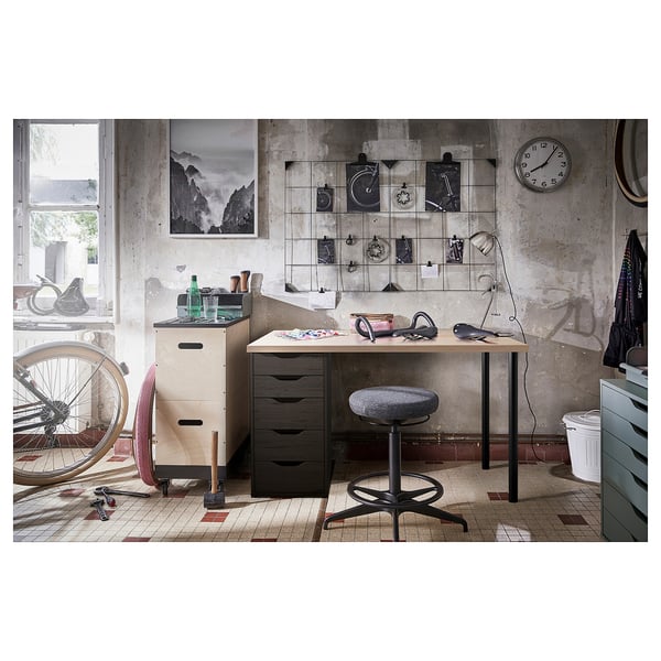 Industrial-style workspace with LAGKAPTEN desk, black drawers, wooden top, bike decor, and hanging clock.