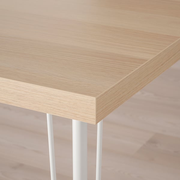 Close-up of light wood tabletop with smooth, even finish and clean, mitered edge, supported by thin metal legs.