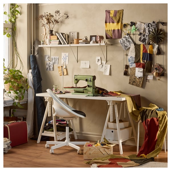 Creative workspace with a white ikea LAGKAPTEN table, green sewing machine, fabric, and decorative items on shelves and wall.