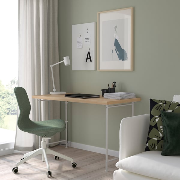 Home office with LAGKAPTEN desk, green chair, white lamp, art, and bed with geometric pillow.