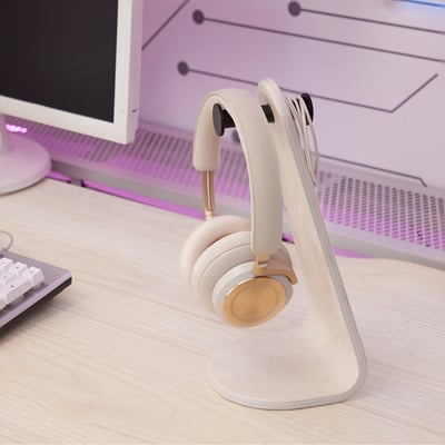 A wooden headset stand holds a white headset on a desk near a computer, keeping the headset organised and easily accessible.
