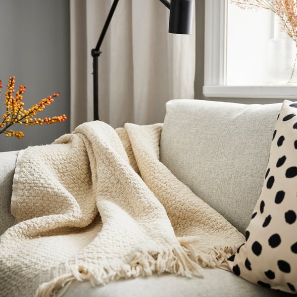 Off-white LAPPTÅG blanket with fringe on sofa.