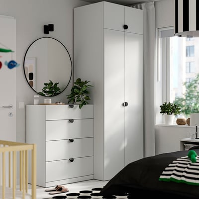 Modern bedroom with white furniture: large wardrobe, 4-drawer chest, crib, and round mirror.