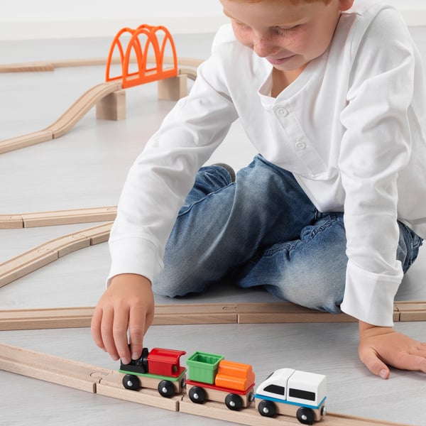 Child playing with magnetic wooden train set, arranging colourful train cars on tracks.