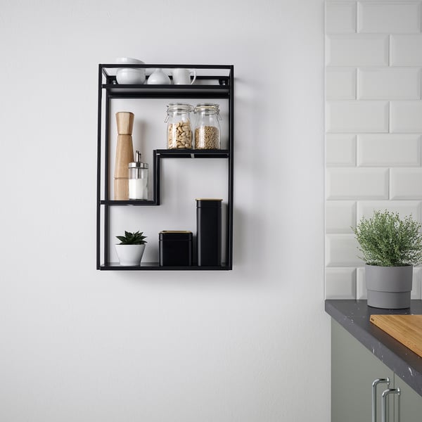 Black shelf with jars, containers, and a plant against a white wall.