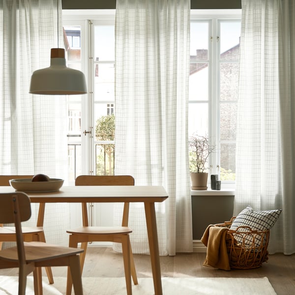 Bright dining room with white grid curtains, wooden table, chairs, and hanging lamp.