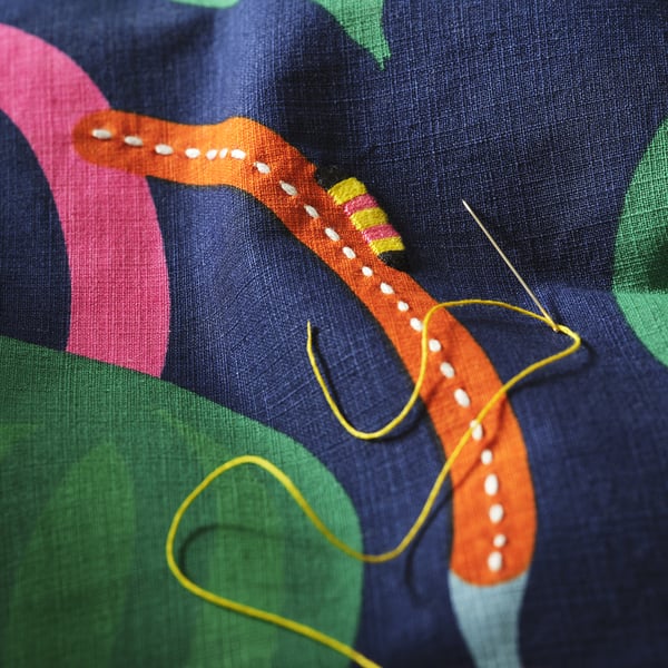 Close-up of hand-embroidered cushion cover showcasing vibrant caterpillar and stitching on abstract fabric.