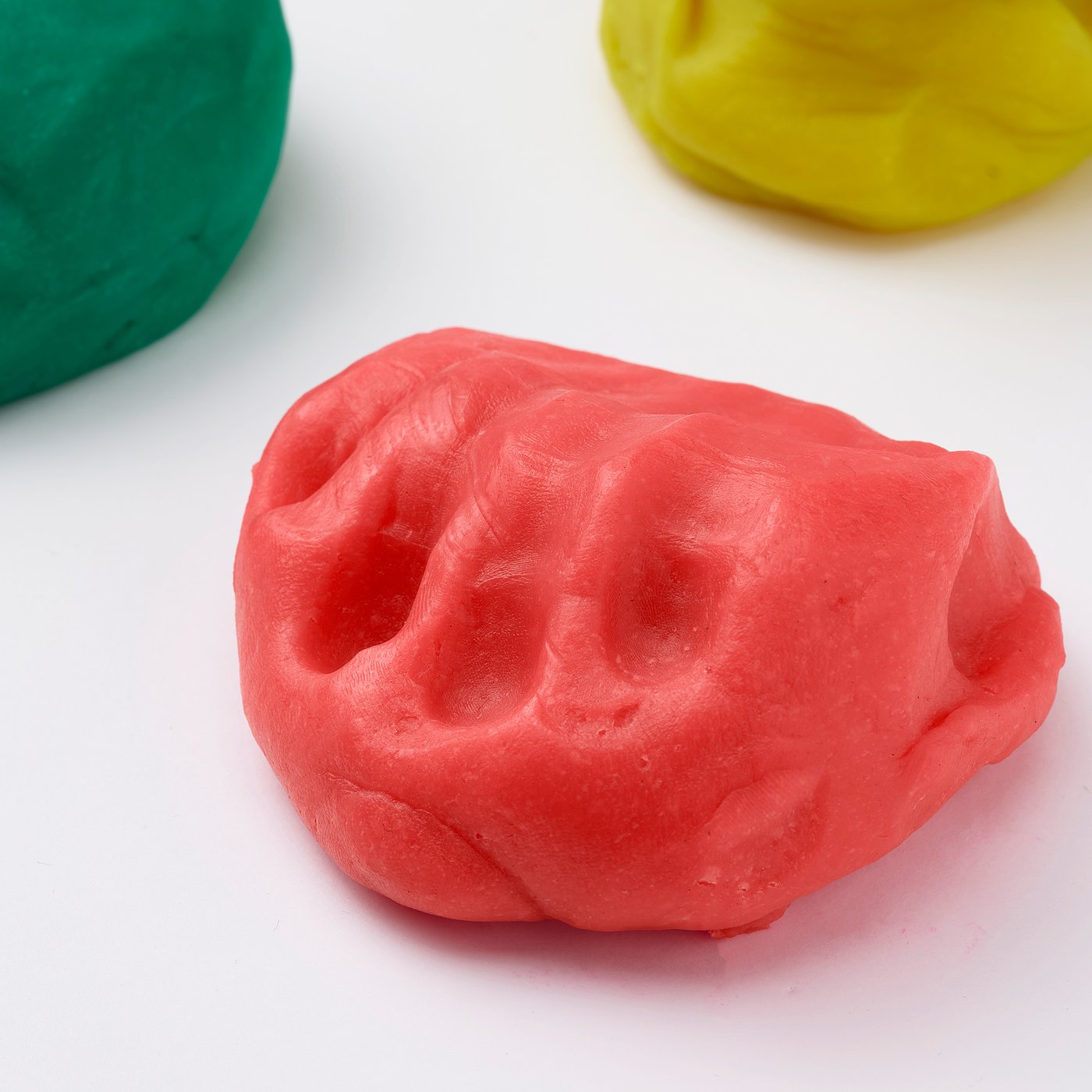 Three blobs of modelling dough in green, red, and yellow on white surface.