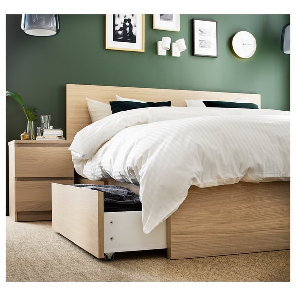 Modern bedroom with light brown MALM bed, white bedding, and drawers. One drawer open showing storage space.