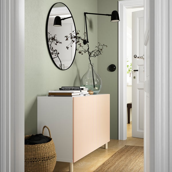 White birch cabinet in hallway, sage green wall, mirror, lamp, books, vase, basket.
