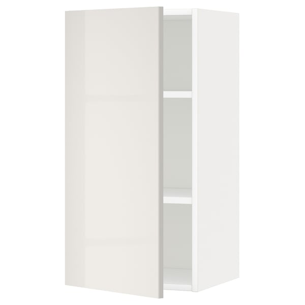 Depicts a white METOD wall cabinet from IKEA, featuring a high gloss finish, with one door slightly open, revealing an adjustable shelf inside.
