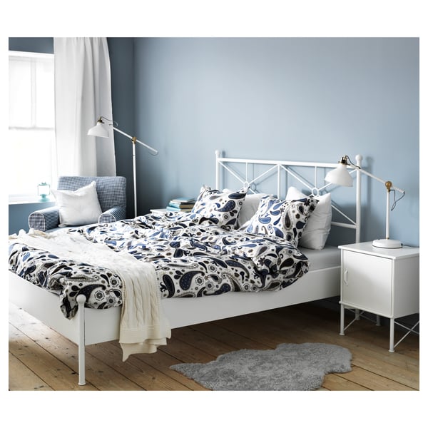 Bedroom with white MUSKEN bedside table, grey rug, patterned bedding on white bed, and blue walls.