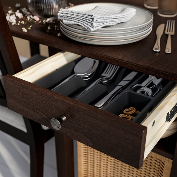 Wooden sideboard drawer with silverware organiser, stackable plates, and cloth napkins.