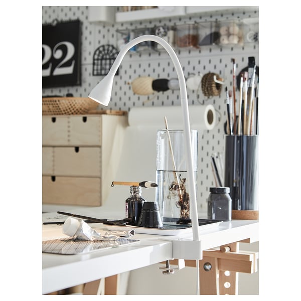 Art studio desk with white adjustable NÄVLINGE lamp, brushes, and supplies.