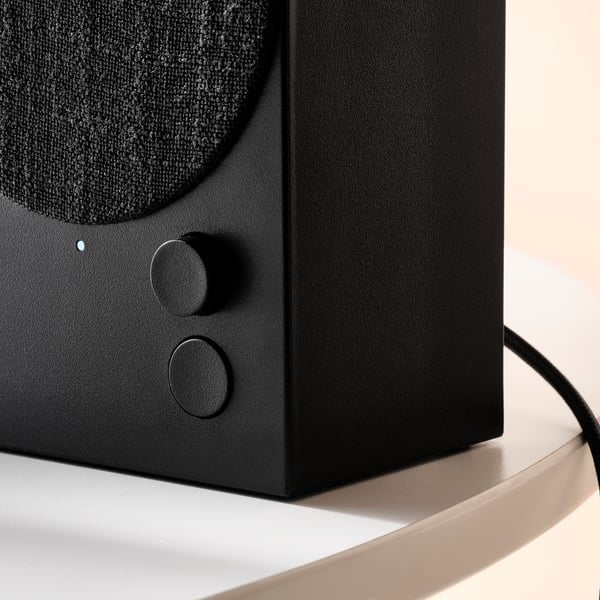 Close-up of a sleek, black bluetooth speaker with textured fabric cover and touch controls, showcasing its high-quality design.