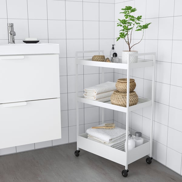 White NISSAFORS 3-tier rolling trolley, compact, with wicker baskets and folded towels for bathroom storage.