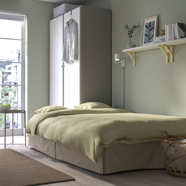 Cosy bedroom with cream sofa-bed, wall-mounted shelves, & closet with hanging garment.