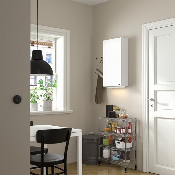 Small kitchen corner with white OMAR cabinet, black chair, and metal spice rack. White door, black lamp, and potted plant by window.