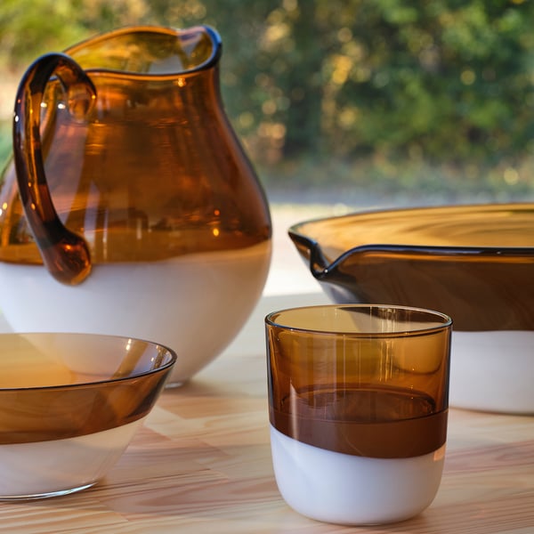 Amber glass cup, with white base, beside large jug on wood table.