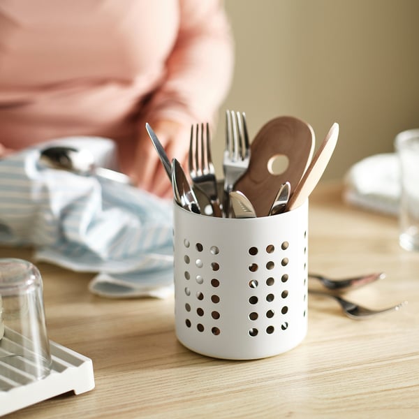 Cutlery in white drying rack, ventilation holes for air flow, sits on wooden table.