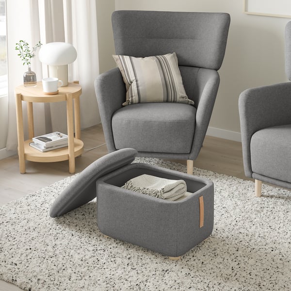Cosy living room with grey OSKARSHAMN wing chairs, a footstool, and side table. The footstool is open, revealing inside storage.