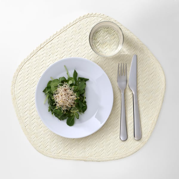 A handwoven palm leaf place mat displaying a salad, knife, fork, and glass, protecting table surfaces and adding natural decor.