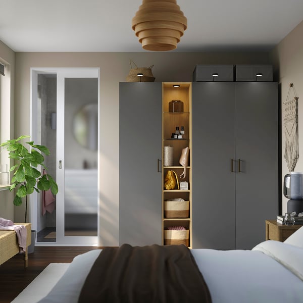 Modern bedroom with dark grey PAX wardrobe, tall plant near glass doors, bed with white & brown covers.