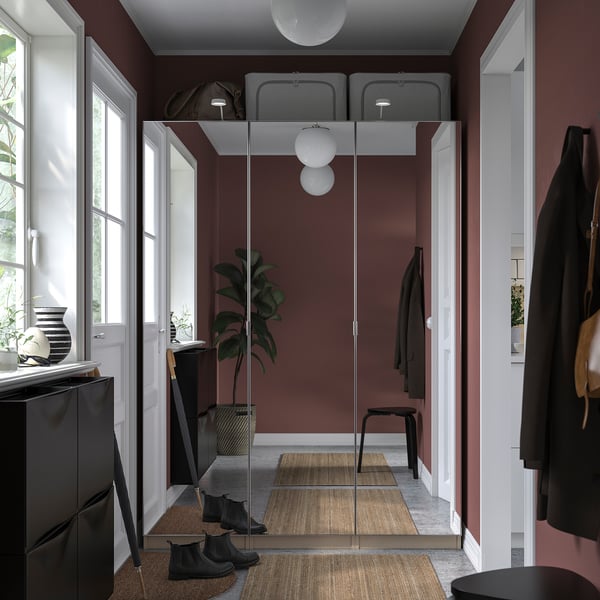 Modern closet with glass doors; dark pink walls; black boots and jackets; hanging & floor plants; two pendant lights.