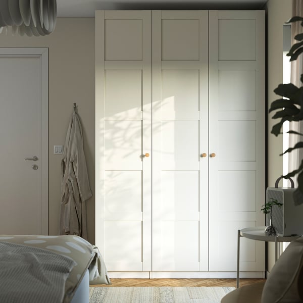 Large white PAX wardrobe with multiple sections next to bed and plant table.