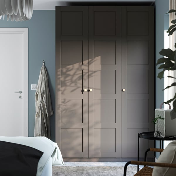 Modern PAX wardrobe, grey, with sunlight patterns, flanked by door and plant.