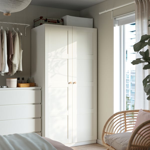 Minimalist bedroom with white PAX wardrobe, silver handles, wicker chair, and simple bed
