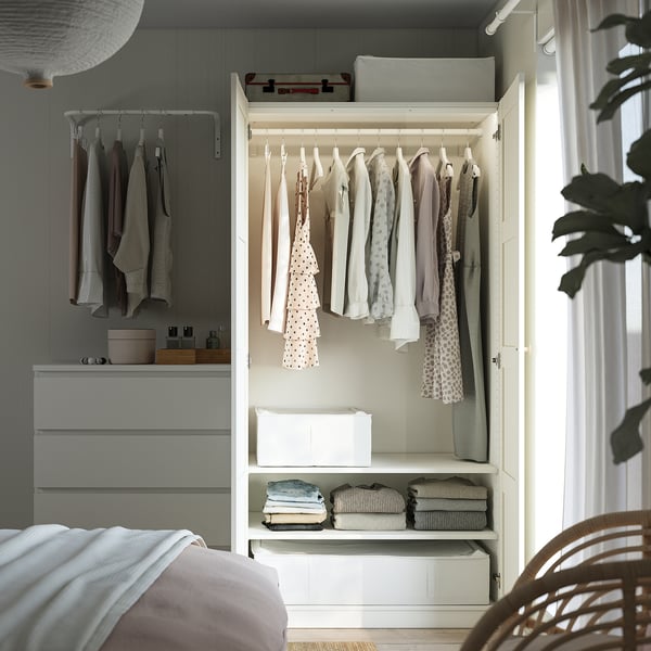 Well-organized bedroom with white PAX wardrobe displaying clothes, folded garments, and storage boxes. Hanging rack on top.