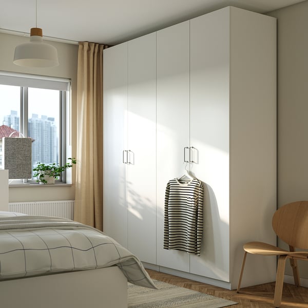 Modern bedroom with large white PAX wardrobe, striped shirt hanging, wooden chair, and bed with a window.