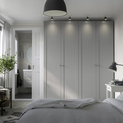Modern grey PAX wardrobe dominates bedroom, towering beside white door, with sleek handles and integrated lighting.
