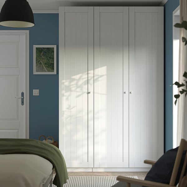 Modern bedroom with large white PAX wardrobe against blue wall, alongside bed, featuring clean lines and plenty of storage space.