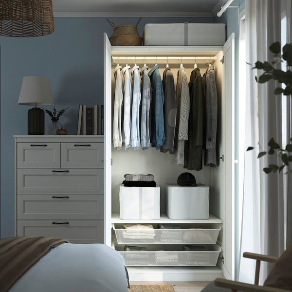 Open closet with clothes on hangers, folded items in baskets, beside drawer units, against blue wall.