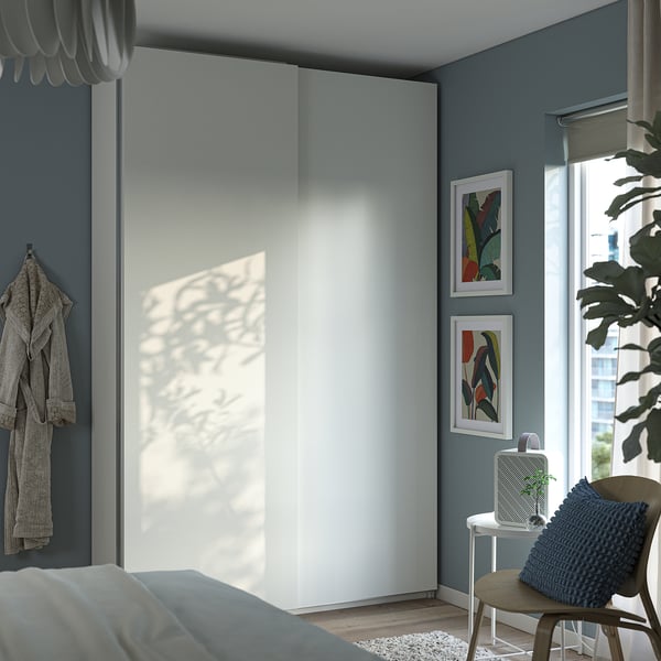 Modern bedroom with large white PAX closet, grey walls, abstract art, cosy chair, blue pillow, plant, and large window.