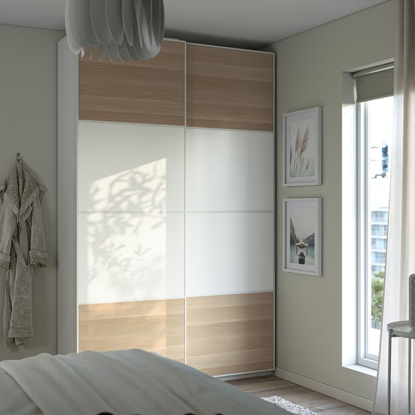 Modern bedroom with white wooden PAX wardrobe, grey robe, and light-colored bedding.