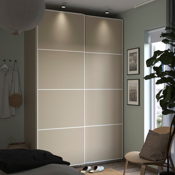 Modern bedroom with beige PAX wardrobe, wooden chair, plant, and wall art.