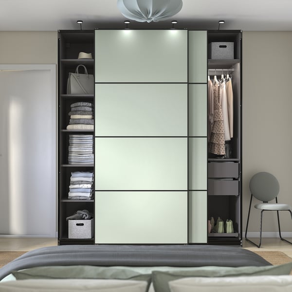 Modern bedroom with light-colored PAX wardrobe featuring shelves, drawers, and hanging space; next to a bed with a green blanket.